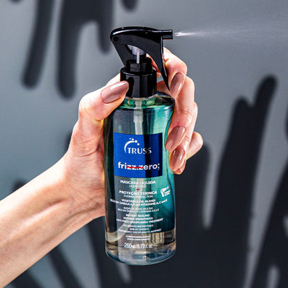 A imagem mostra uma mão segurando um frasco de máscara líquida para cabelos da marca Truss, linha "frizz zero". O frasco é transparente, permitindo ver o conteúdo no interior.
